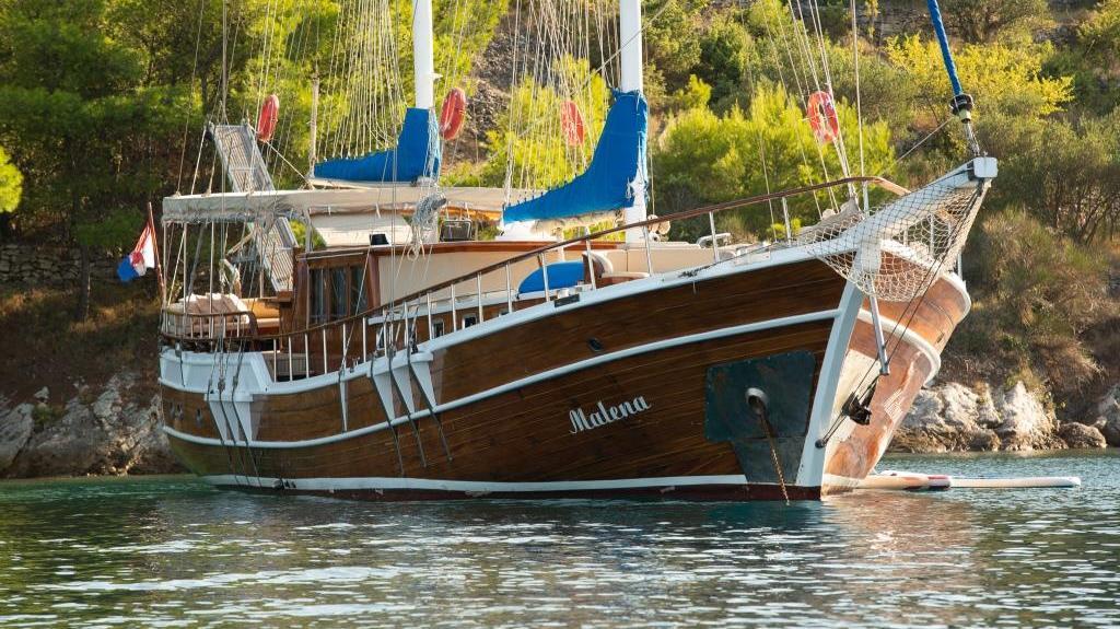 Traditional wooden gulet yacht Malena with blue sails anchored in Mediterranean bay