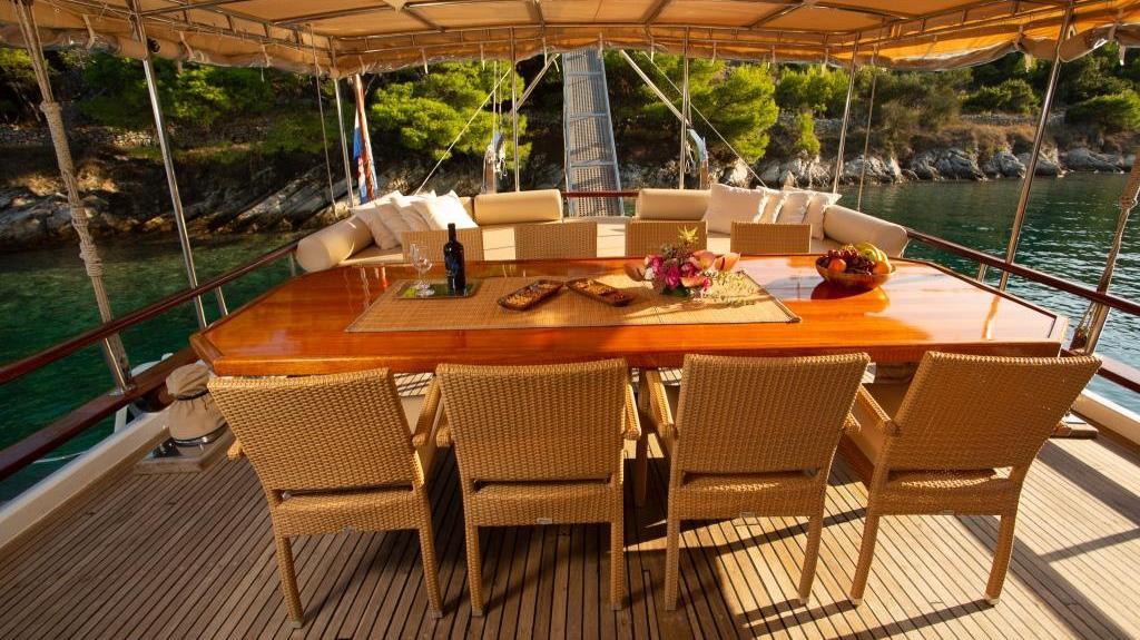 Gulet aft deck dining table with wicker chairs anchored in Mediterranean bay