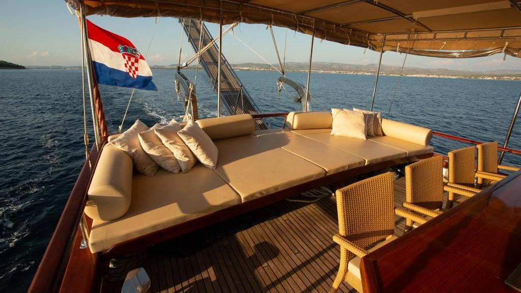 Gulet yacht aft deck with convertible seating and Croatian flag underway