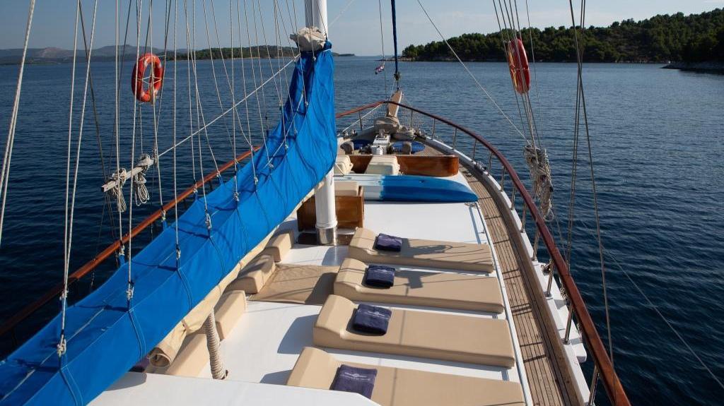 gulet yacht forward deck with sunbathing mattresses and blue sail