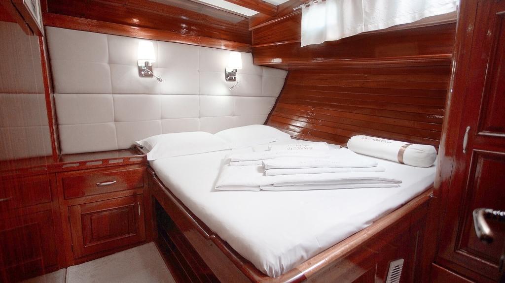 Luxury yacht cabin with double bed, mahogany wood paneling and white linens
