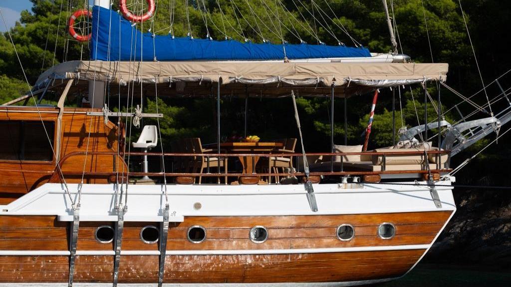 Traditional wooden gulet yacht with outdoor dining area moored in forested bay