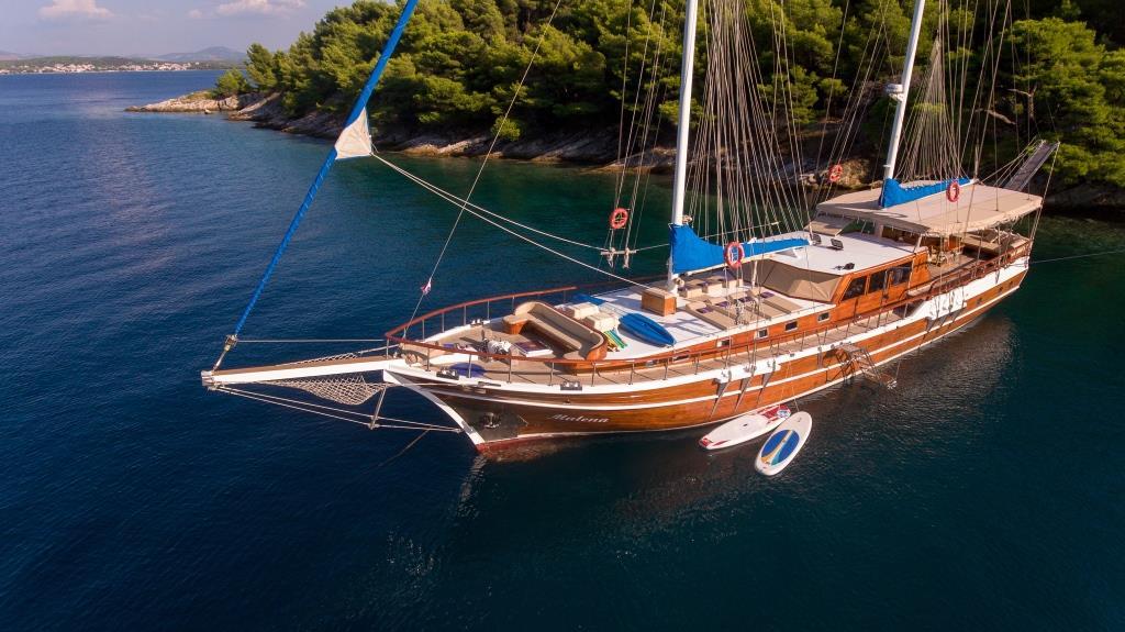 Traditional wooden gulet yacht anchored in turquoise Mediterranean bay near pine forest