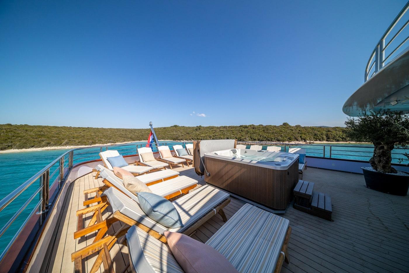 Luxury yacht upper deck featuring jacuzzi hot tub and white sun loungers
