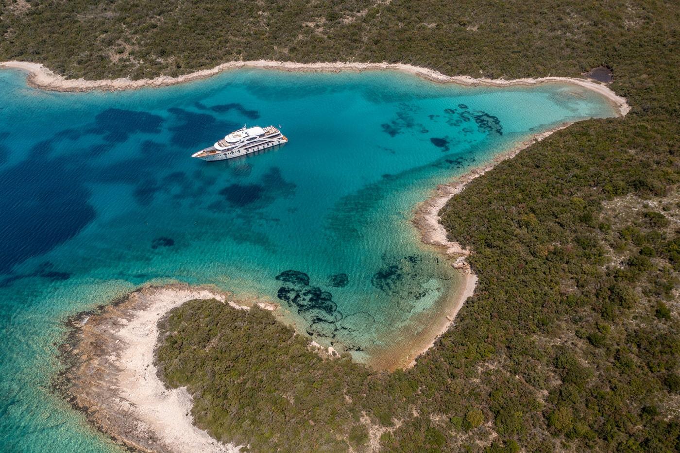 White luxury yacht anchored in pristine turquoise bay surrounded by green coastline