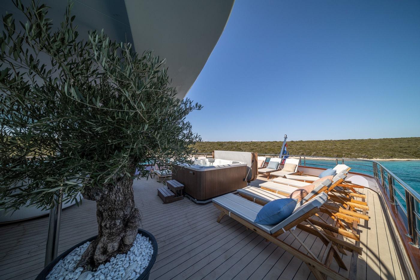 luxury yacht upper deck featuring jacuzzi, teak sun loungers and olive tree