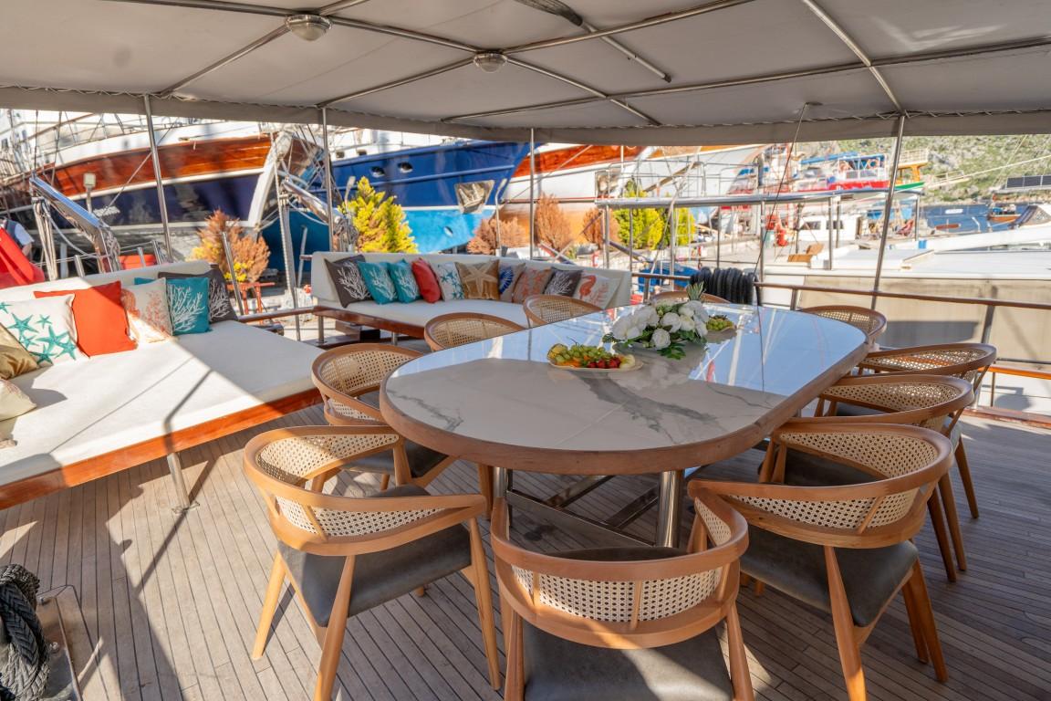 yacht aft deck dining area with round table, wicker chairs under canvas awning