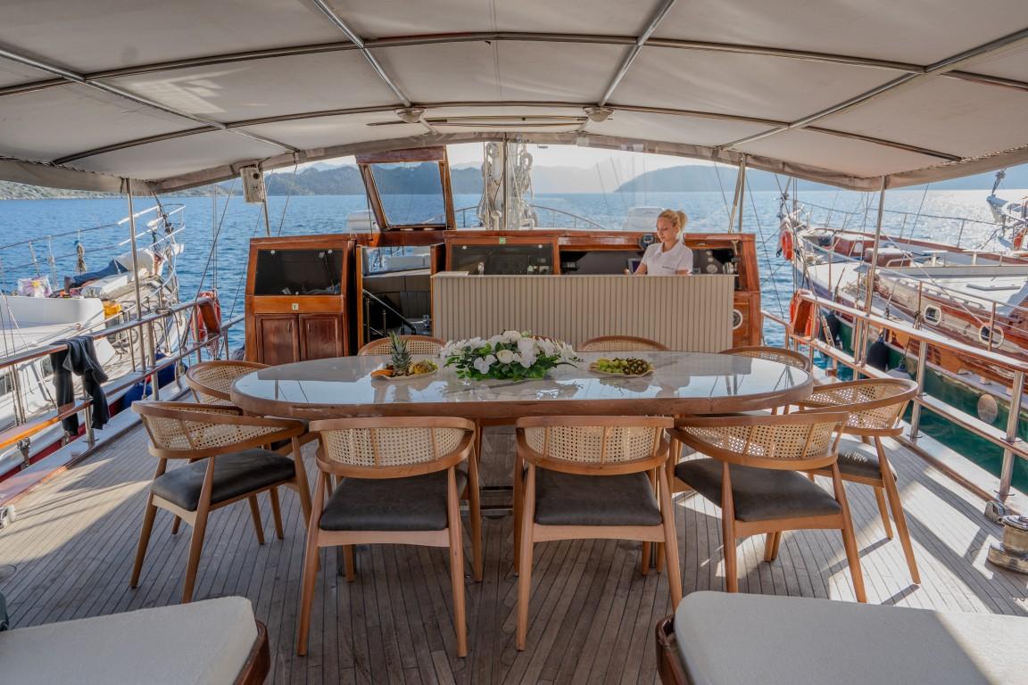 covered aft deck with oval dining table, wicker chairs, and crew member in background