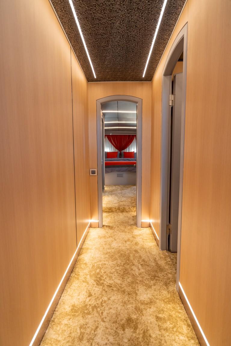 yacht interior corridor with warm lighting leading to guest cabin with red bedding