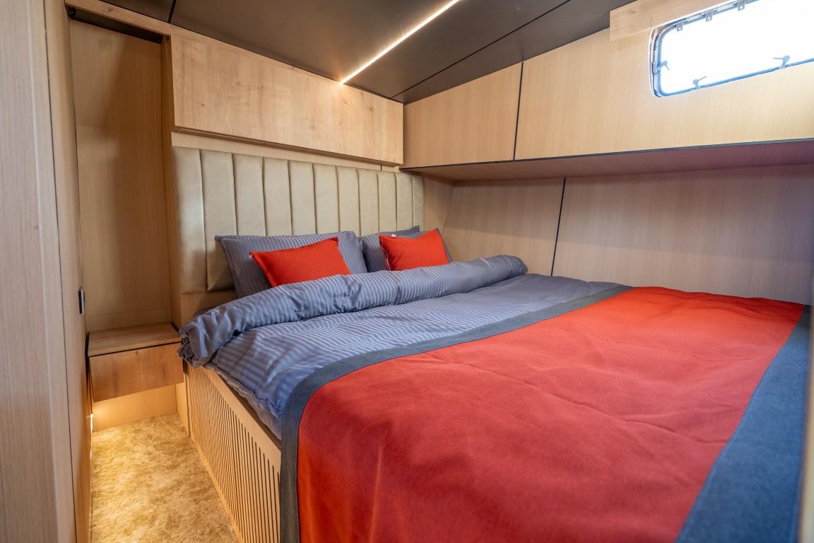 yacht guest cabin featuring double bed with orange and blue bedding, cream upholstered headboard