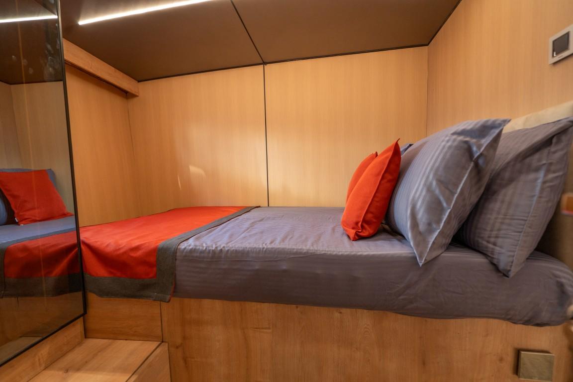 yacht guest cabin featuring twin beds with orange and gray bedding and mirrored wardrobe
