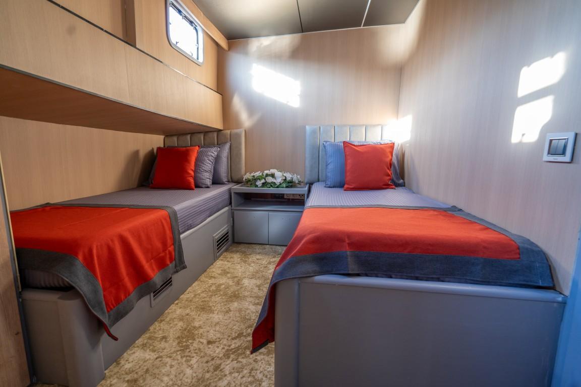 yacht twin cabin with two single beds, red throws, and light wood paneling