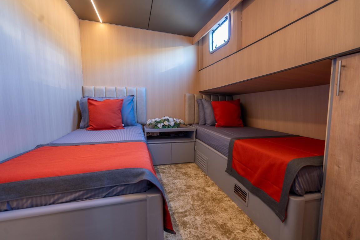 guest cabin with two single beds, red throws, white upholstered headboards and porthole window
