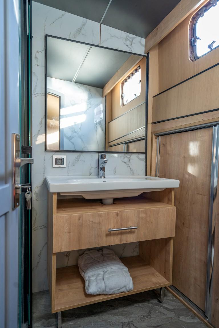 yacht bathroom featuring white sink, wooden vanity with drawer, mirror and marble walls