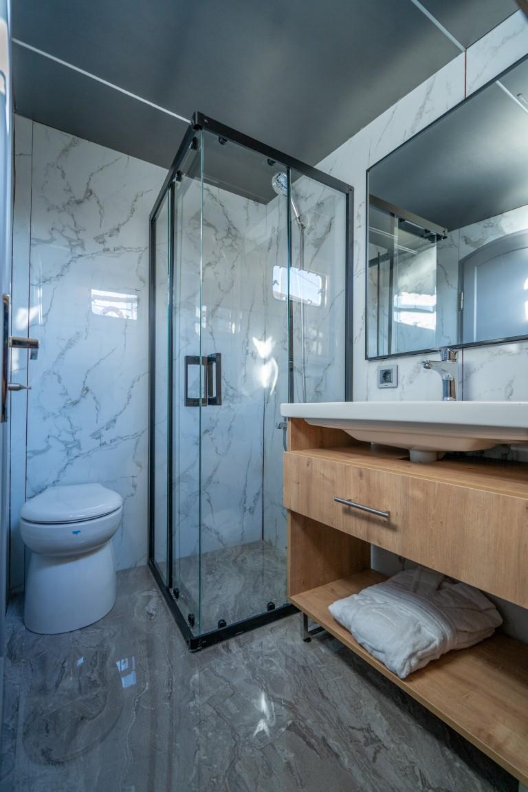 luxury yacht bathroom featuring glass shower enclosure, marble walls, wooden vanity and toilet
