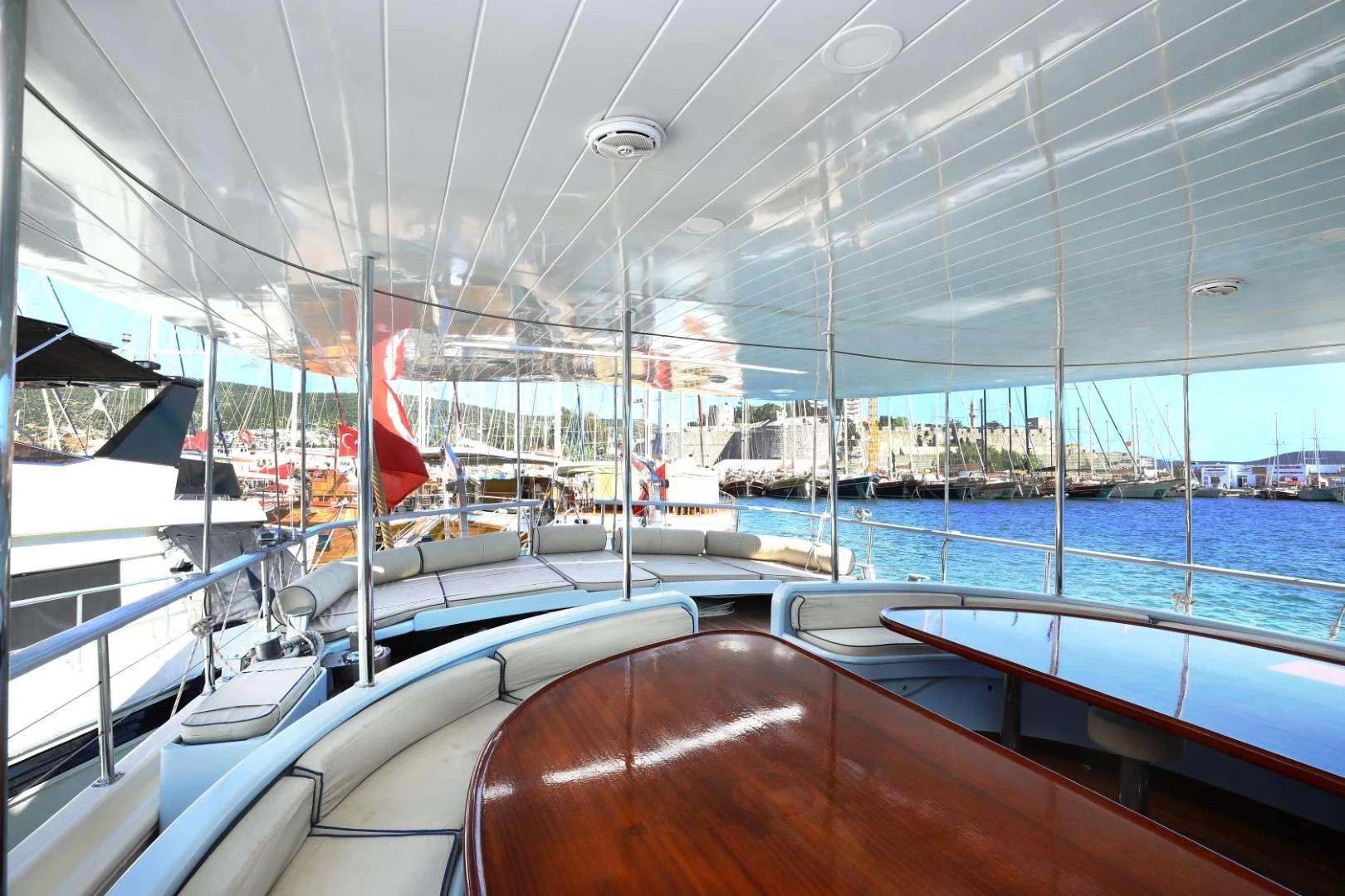 yacht aft deck with curved seating, polished wood dining table and marina views