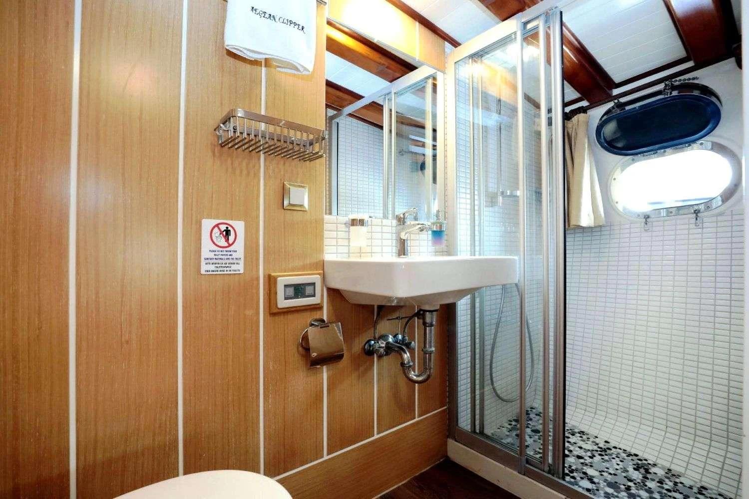 yacht bathroom with white sink, glass shower enclosure and wood paneling