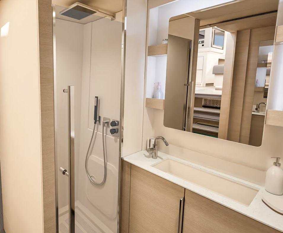 Yacht en-suite bathroom with glass-enclosed overhead rain shower, integrated vanity basin, light wood cabinetry and large mirror