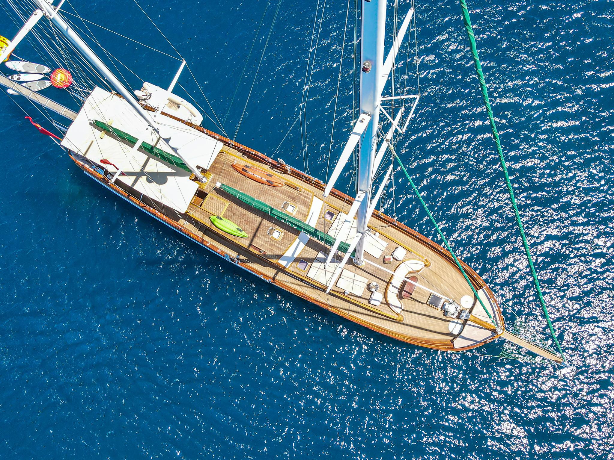 aerial view of luxury sailing yacht with wooden deck and white sails anchored in deep blue water