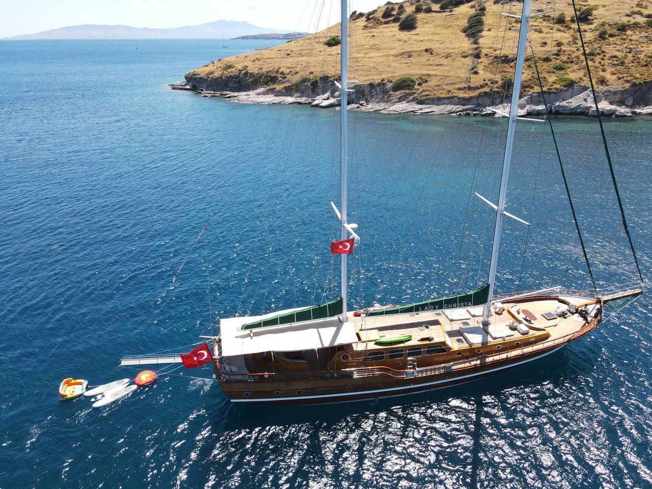 Aerial view of traditional wooden gulet yacht anchored in crystal clear turquoise waters near golden coastline