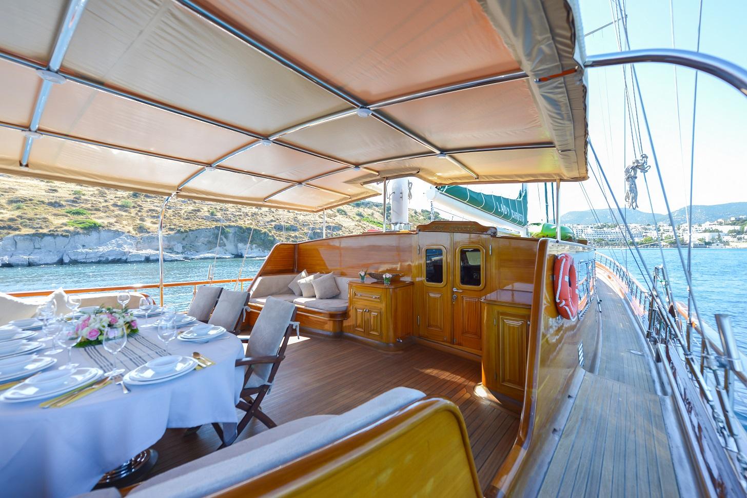 gulet aft deck with outdoor dining table, cushioned seating area and retractable awning