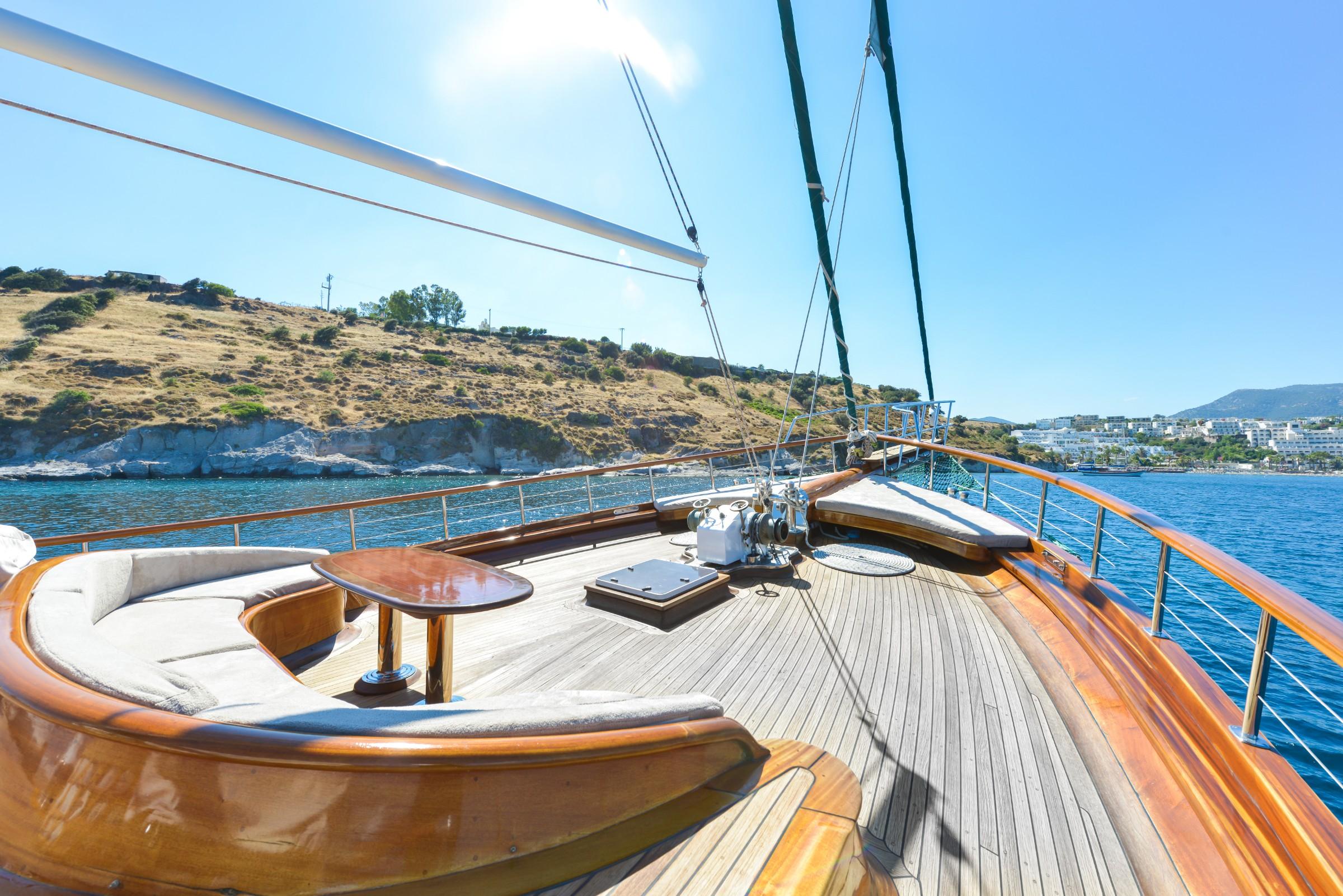 forward deck lounge area with curved white cushioned seating and teak decking underway