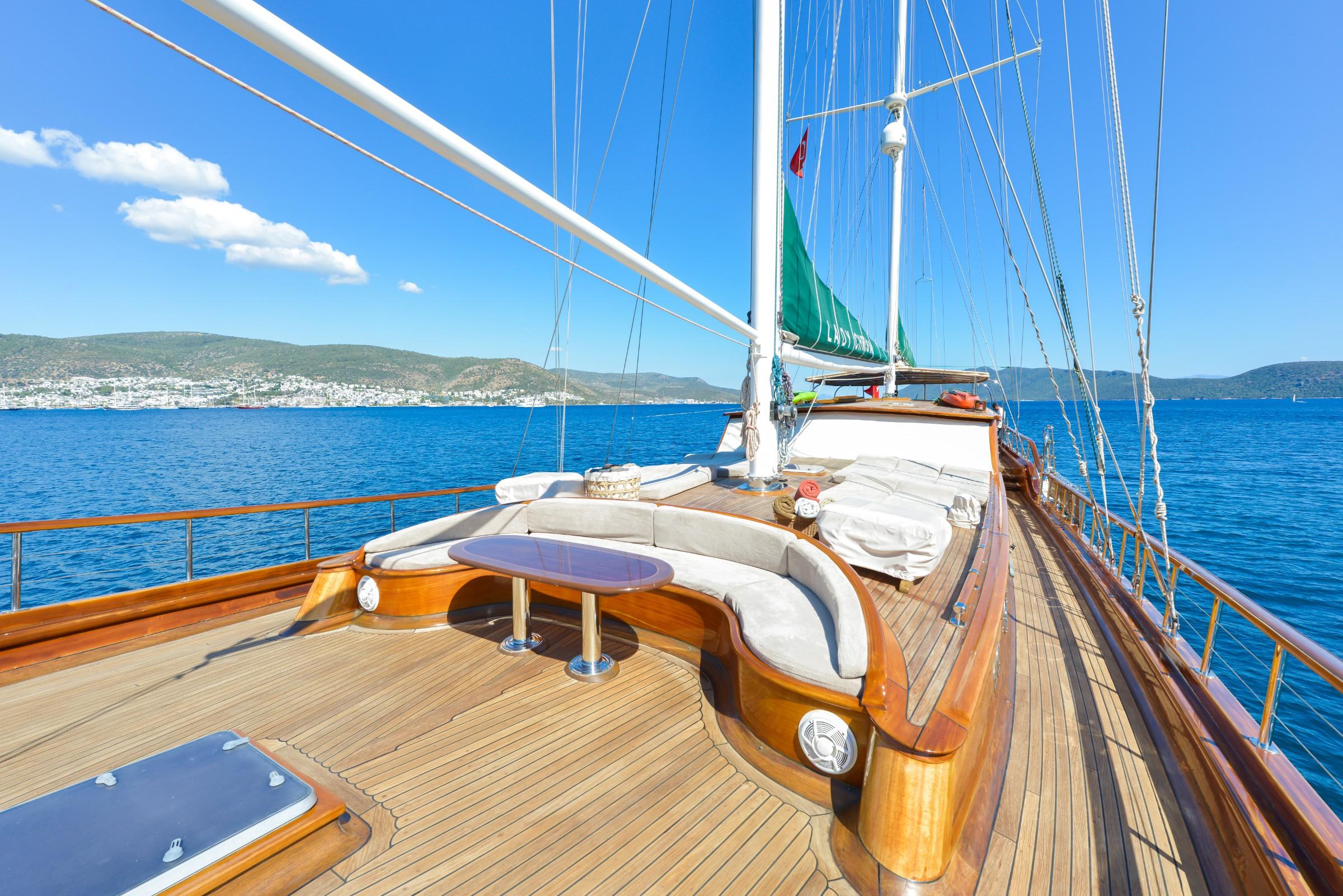 wooden gulet bow deck with curved seating area, teak decking and white mast rigging