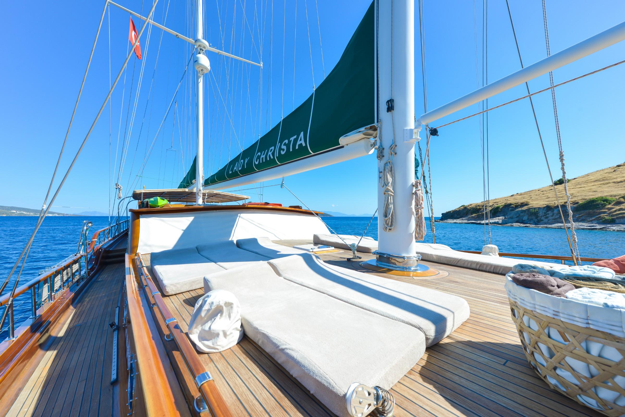 bow deck with white cushioned sunbathing loungers and traditional sailing rigging