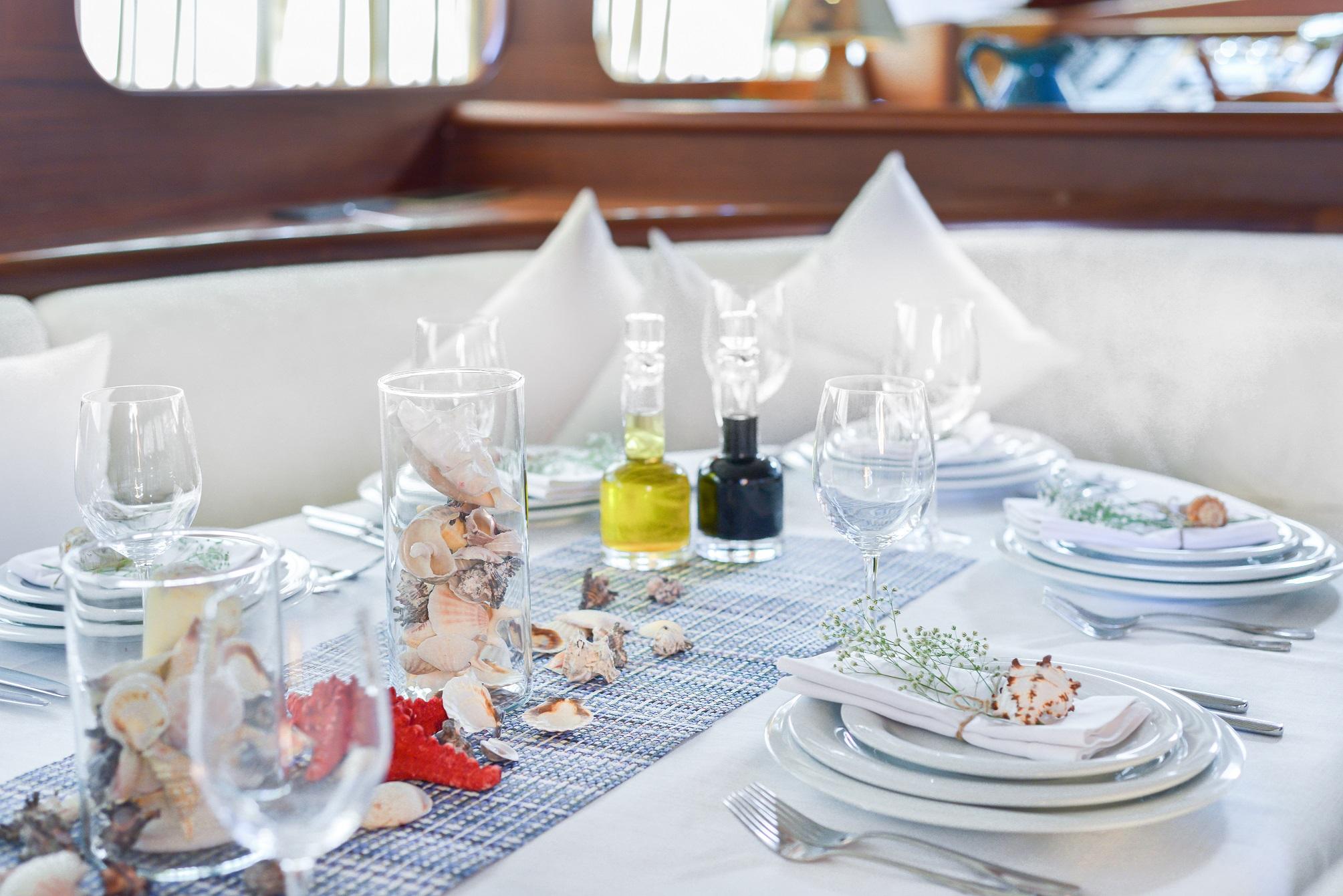 yacht dining table set with white plates, wine glasses, seashells and olive oil bottles