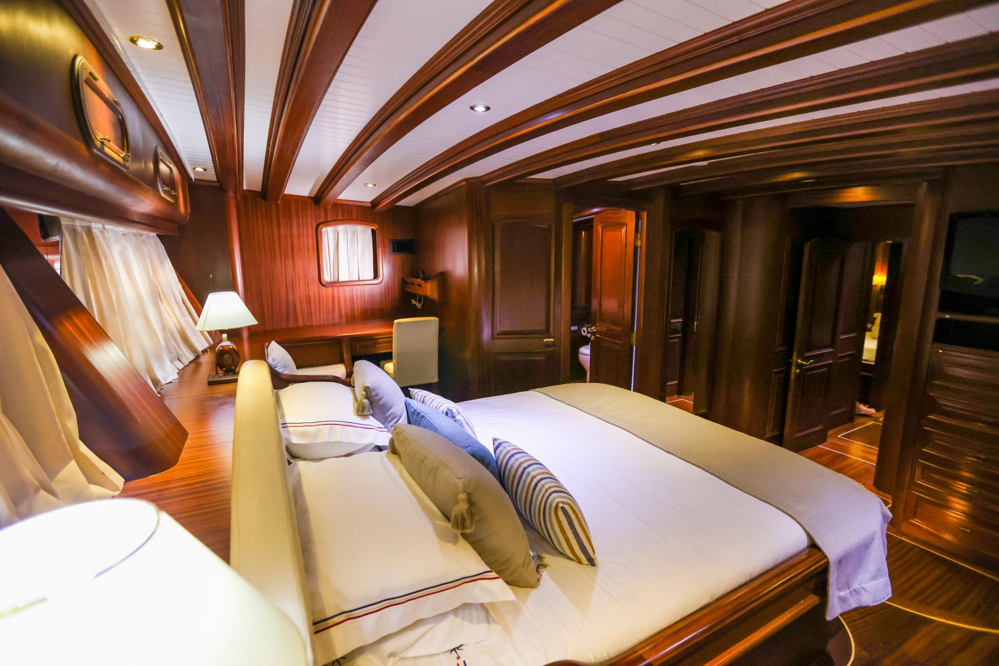 Master cabin interior with king bed, wood paneling, porthole window and built-in wardrobes