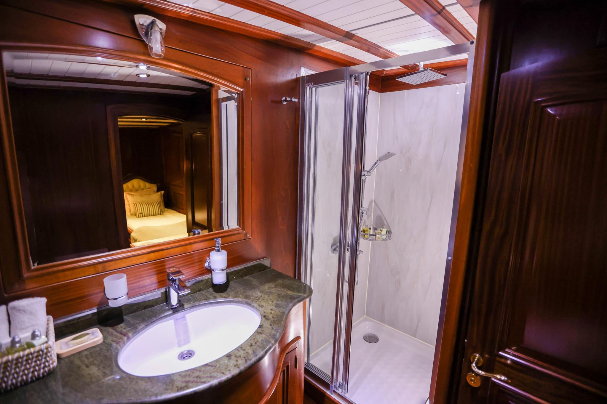 yacht cabin en-suite bathroom with marble vanity, mirror, and glass shower enclosure