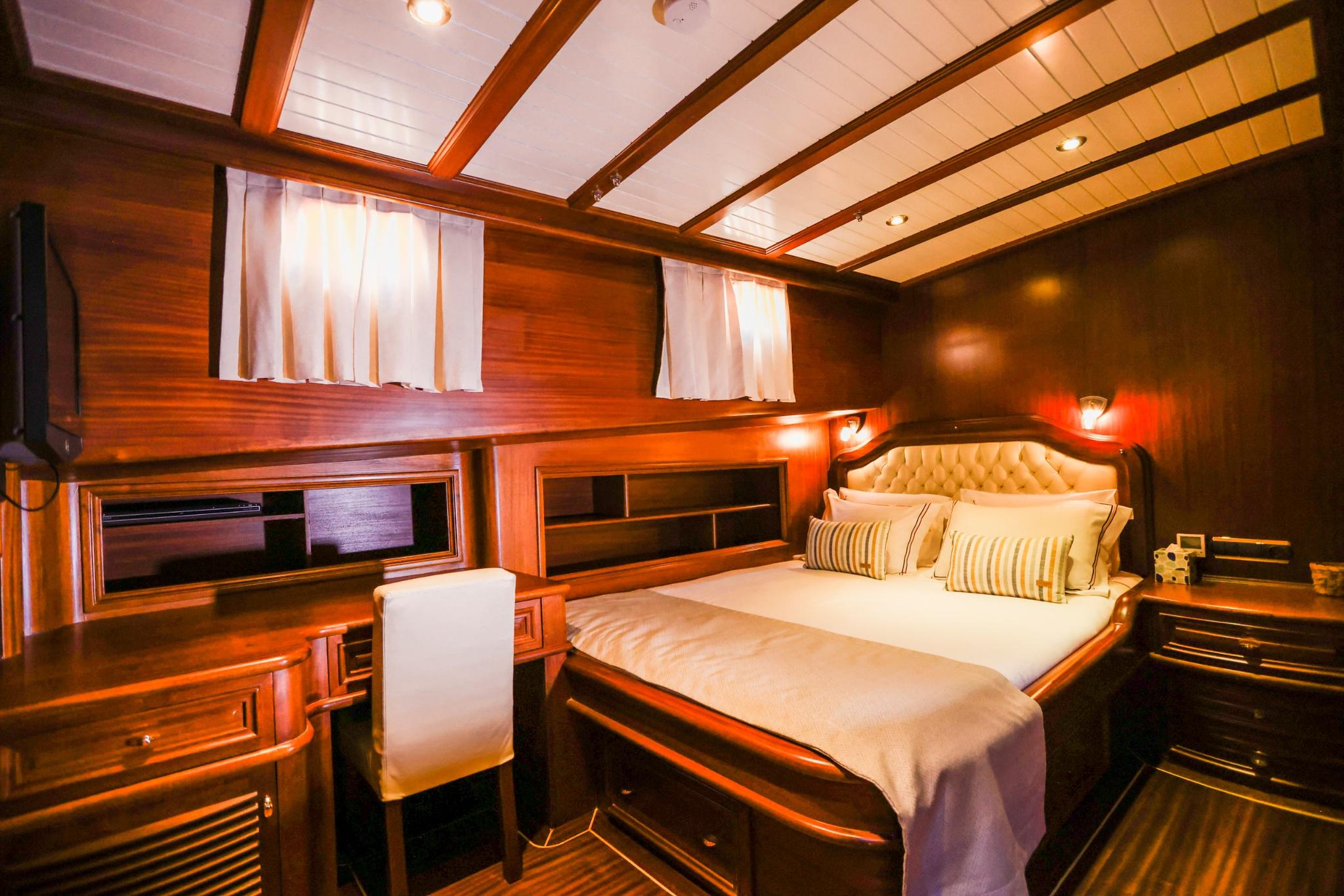 yacht guest cabin with double bed, wooden paneling, desk area and two portholes