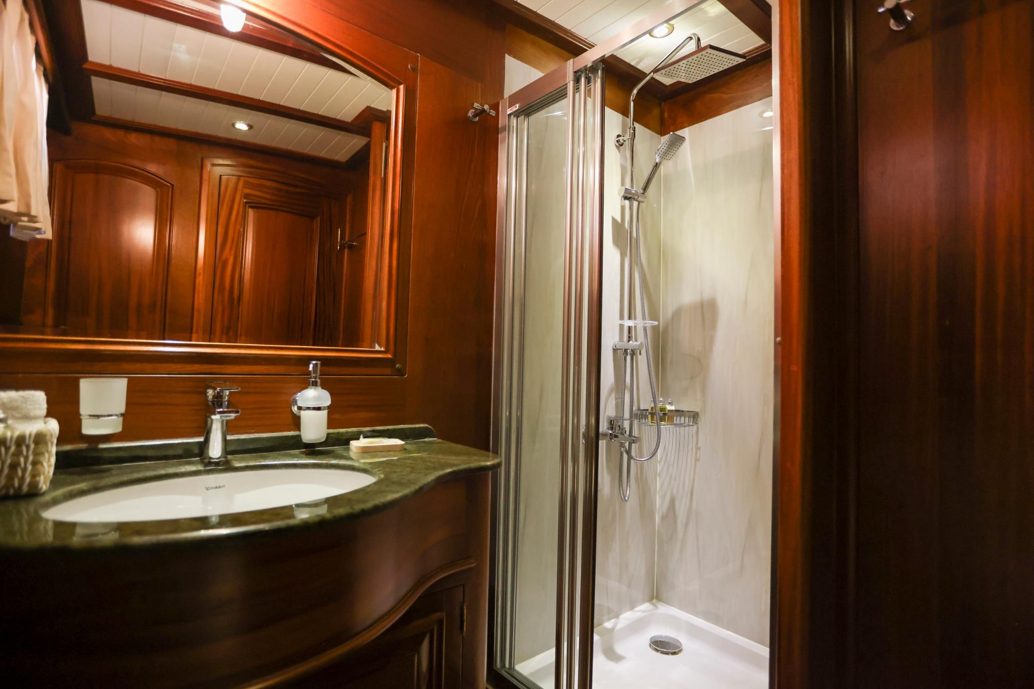 luxury yacht bathroom featuring marble vanity, mirror, glass shower enclosure with chrome fixtures