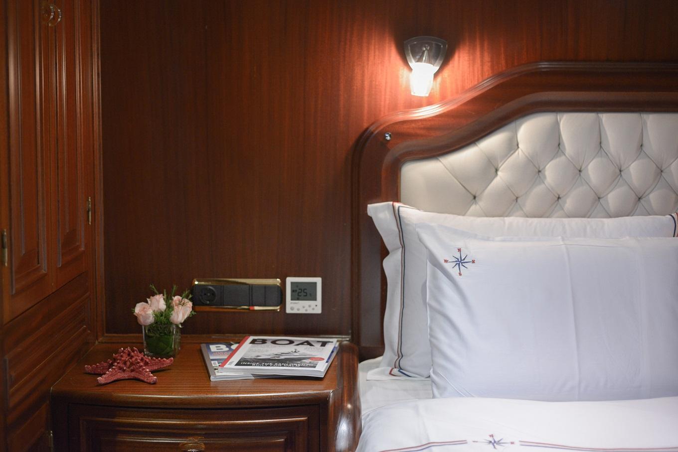 yacht cabin with tufted white leather headboard, wooden bedside table and nautical linens