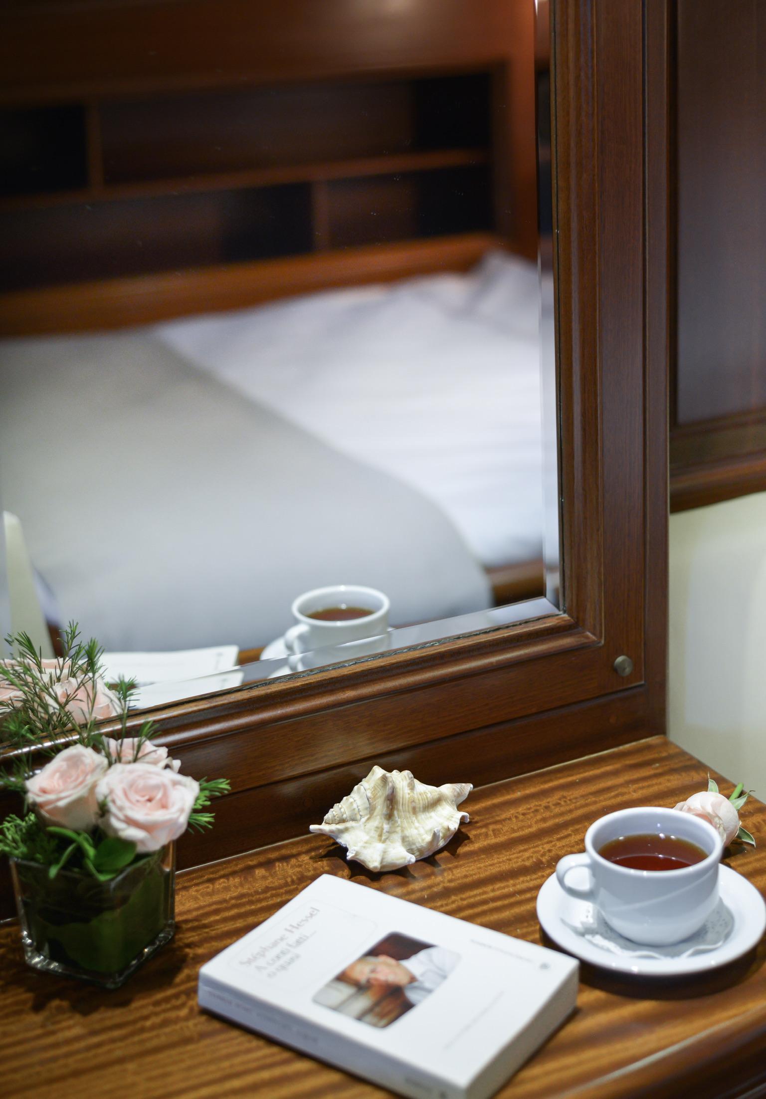 yacht cabin interior showing bed with white linens reflected in wooden-framed mirror