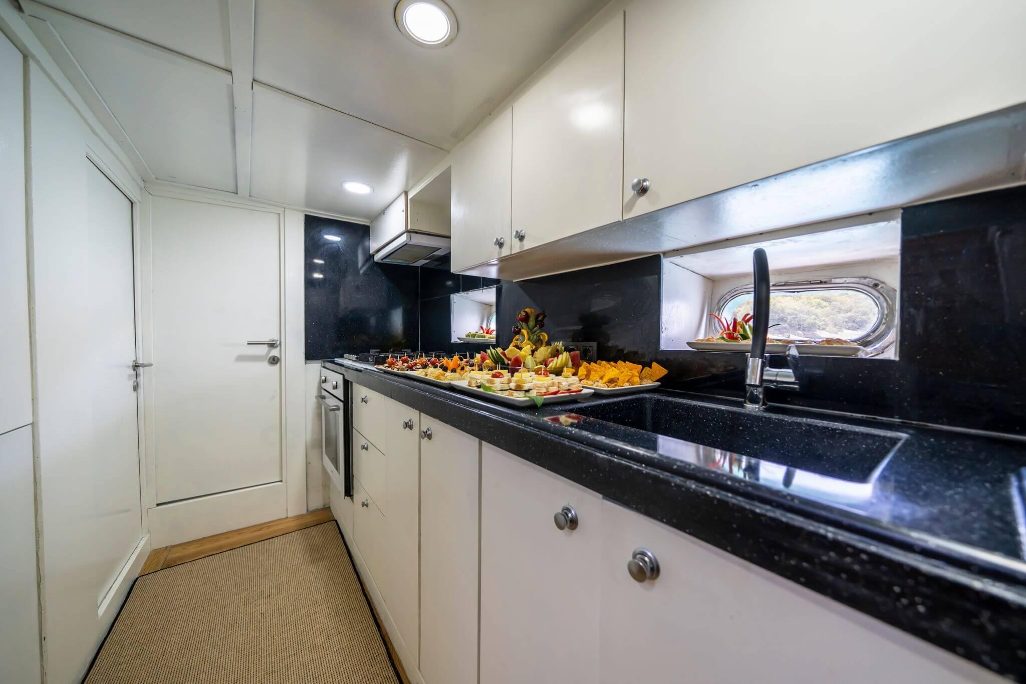 Gulet galley kitchen with black granite worktop displaying trays of canapes, cheese, fruit and snacks ready to serve