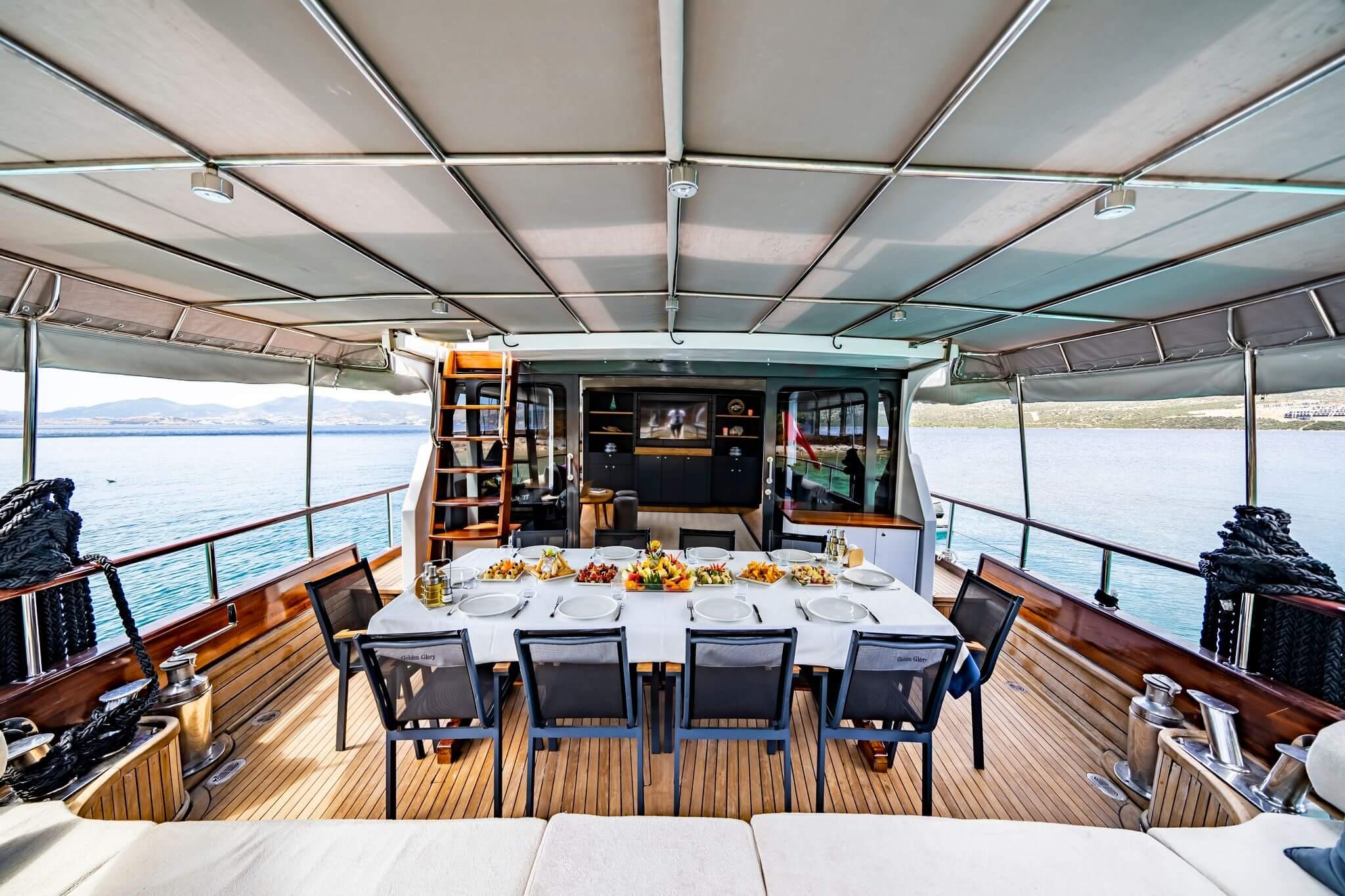 Gulet aft deck dining table set for eight guests with fresh fruit and mezze platters under shade canopy