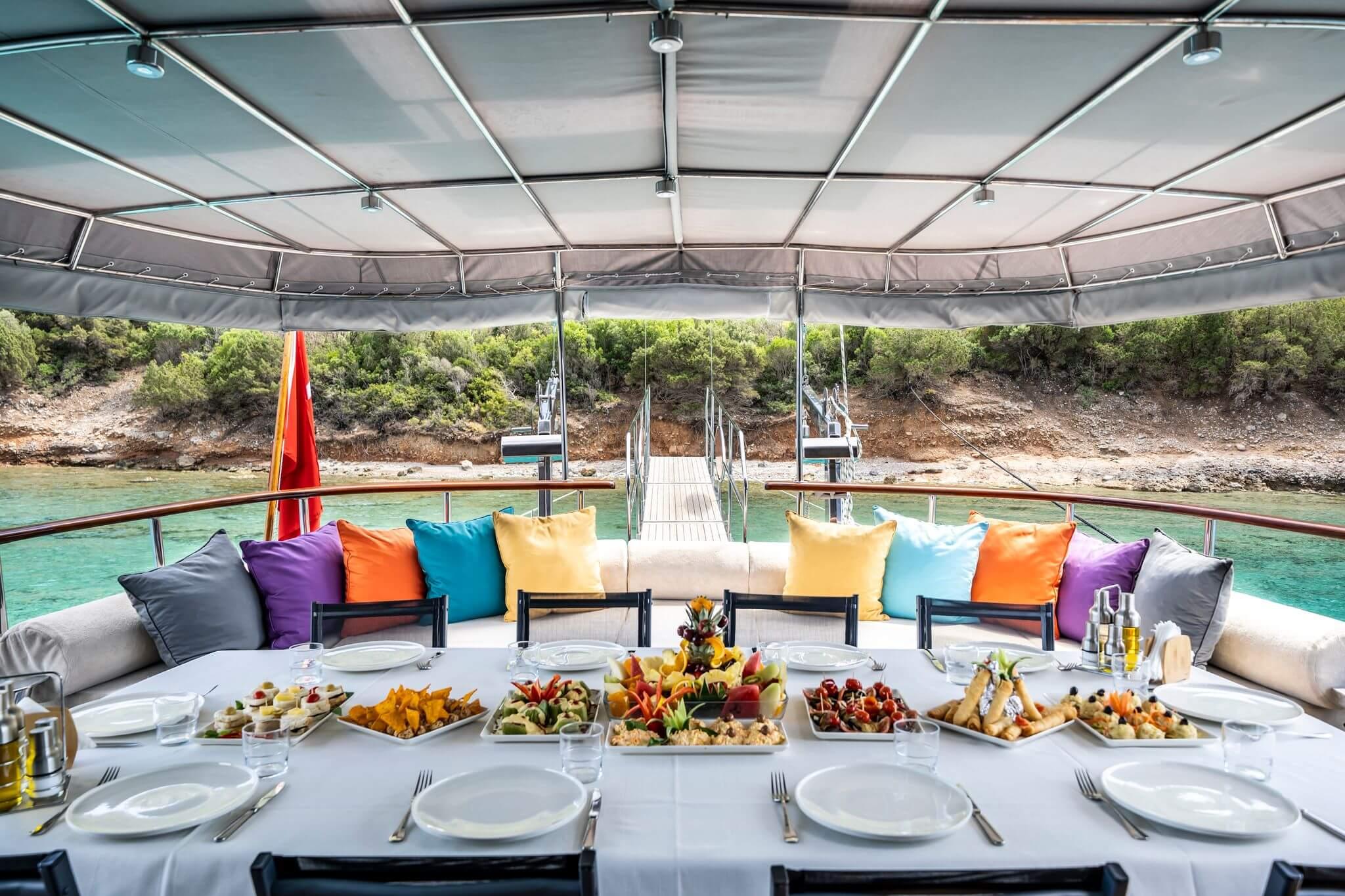 gulet aft deck dining table set with colourful mezze platters and place settings, moored in turquoise cove