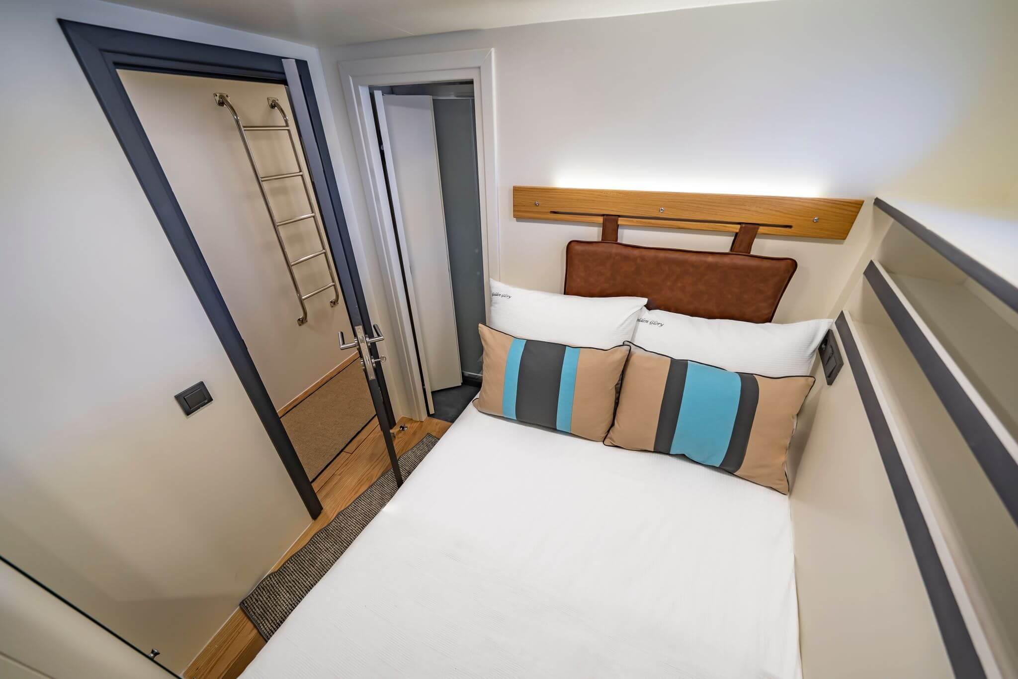 Compact yacht guest cabin with white bedding, striped cushions, leather headboard, and en-suite doorway