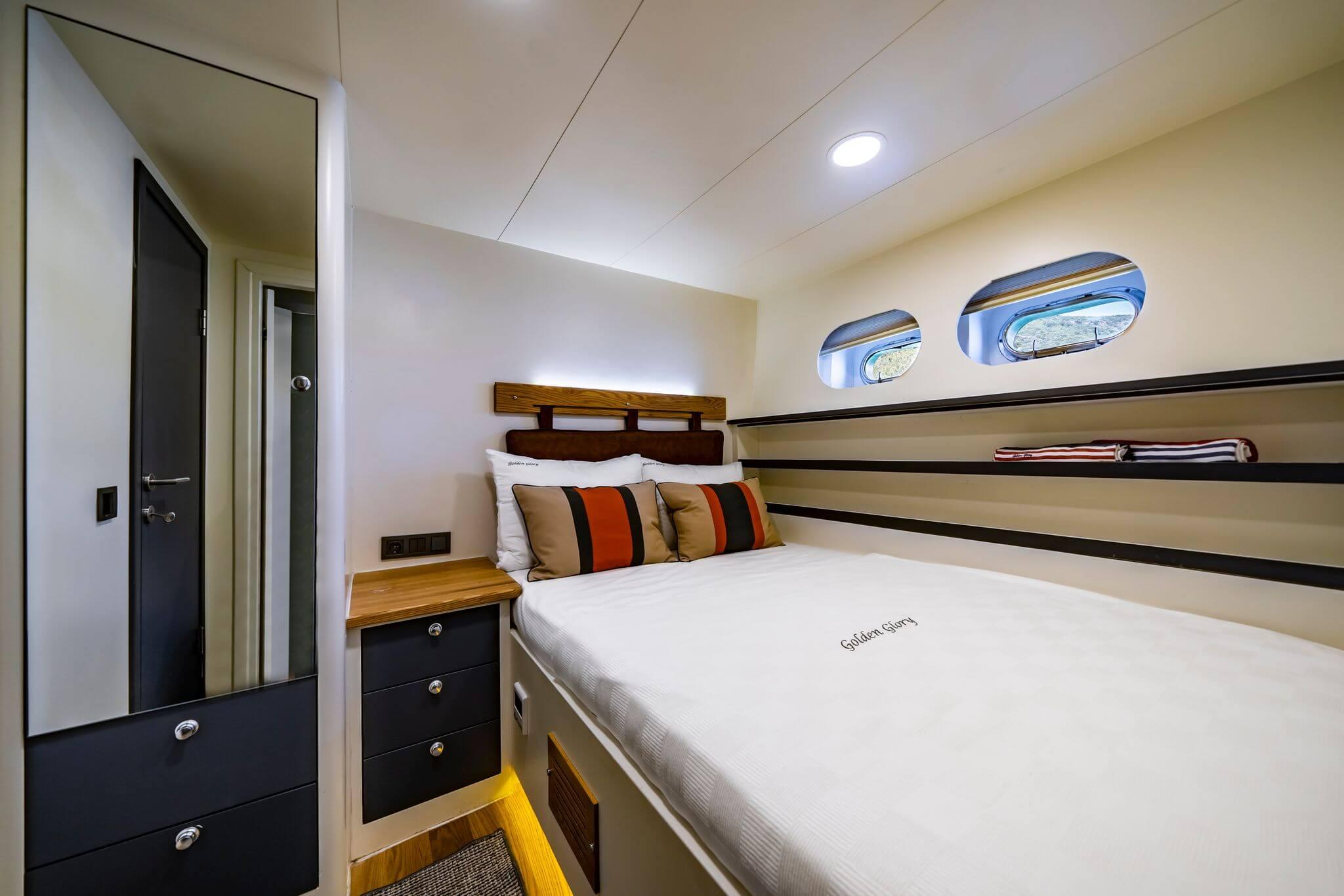 Golden Glory gulet double cabin with striped cushions, wood headboard, and two oval portholes