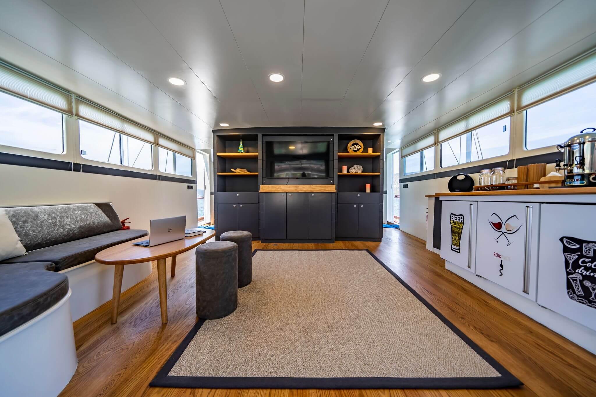 Gulet main saloon with dark wood entertainment unit, flat screen TV, bar counter, and seating area