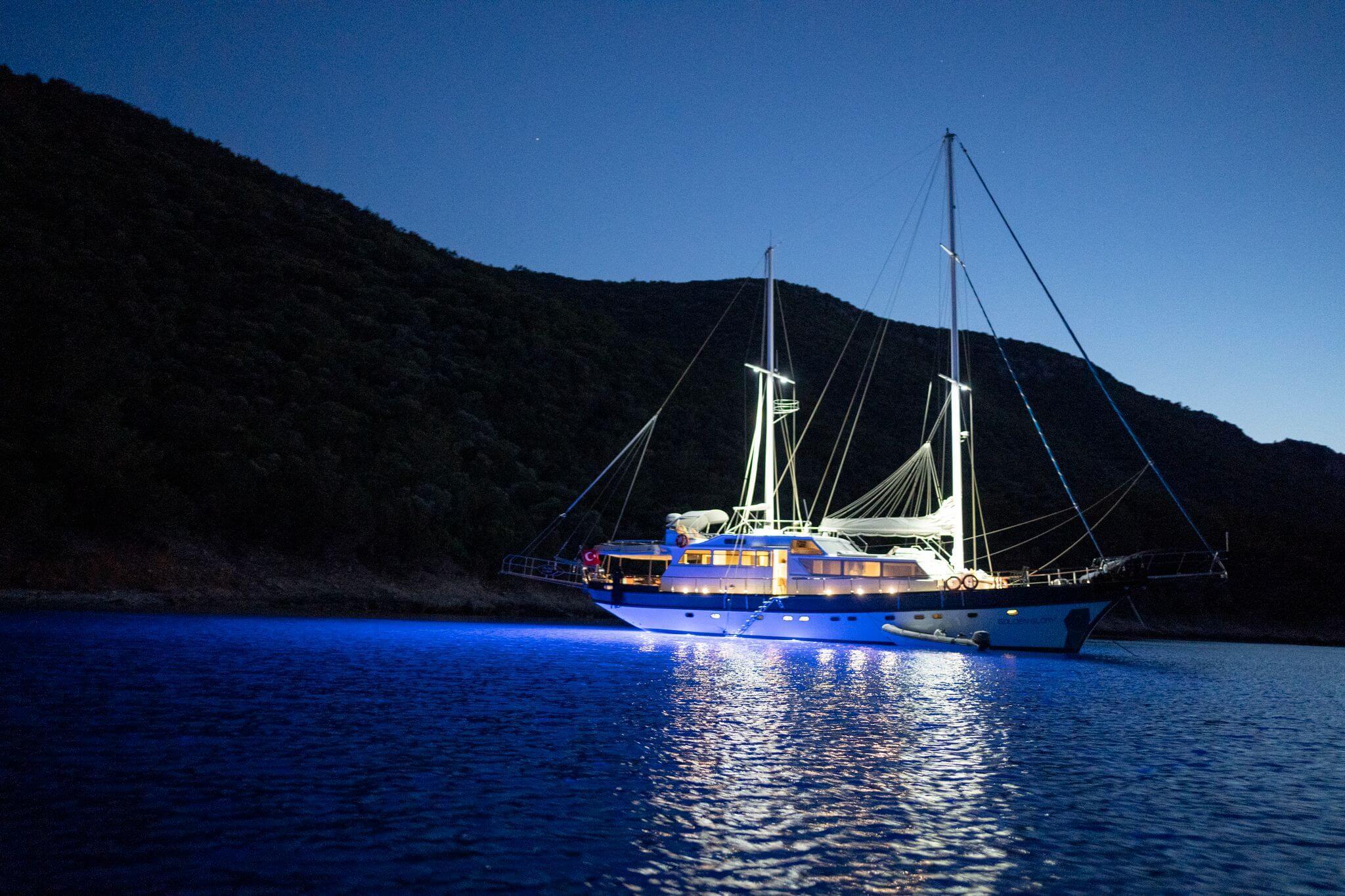 luxury gulet anchored in calm cove at night with glowing blue underwater hull lights