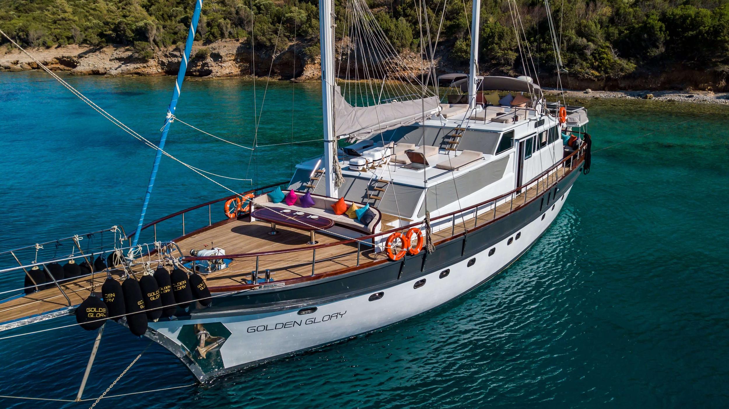Aerial view of gulet Golden Glory anchored in crystal-clear turquoise cove with teak decks and colourful bow cushions