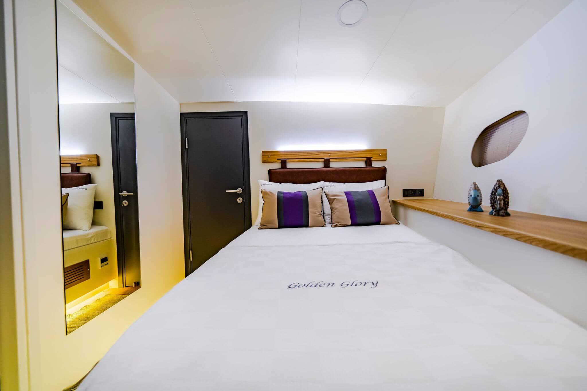 Golden Glory gulet double cabin with leather headboard, branded white duvet, and striped purple-grey cushions