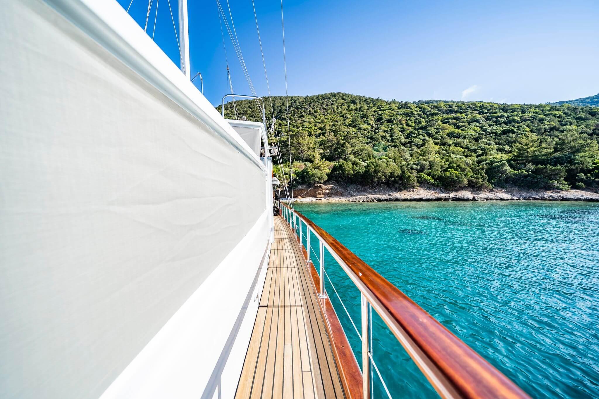 gulet starboard side deck with teak planking and varnished wood handrail overlooking turquoise bay