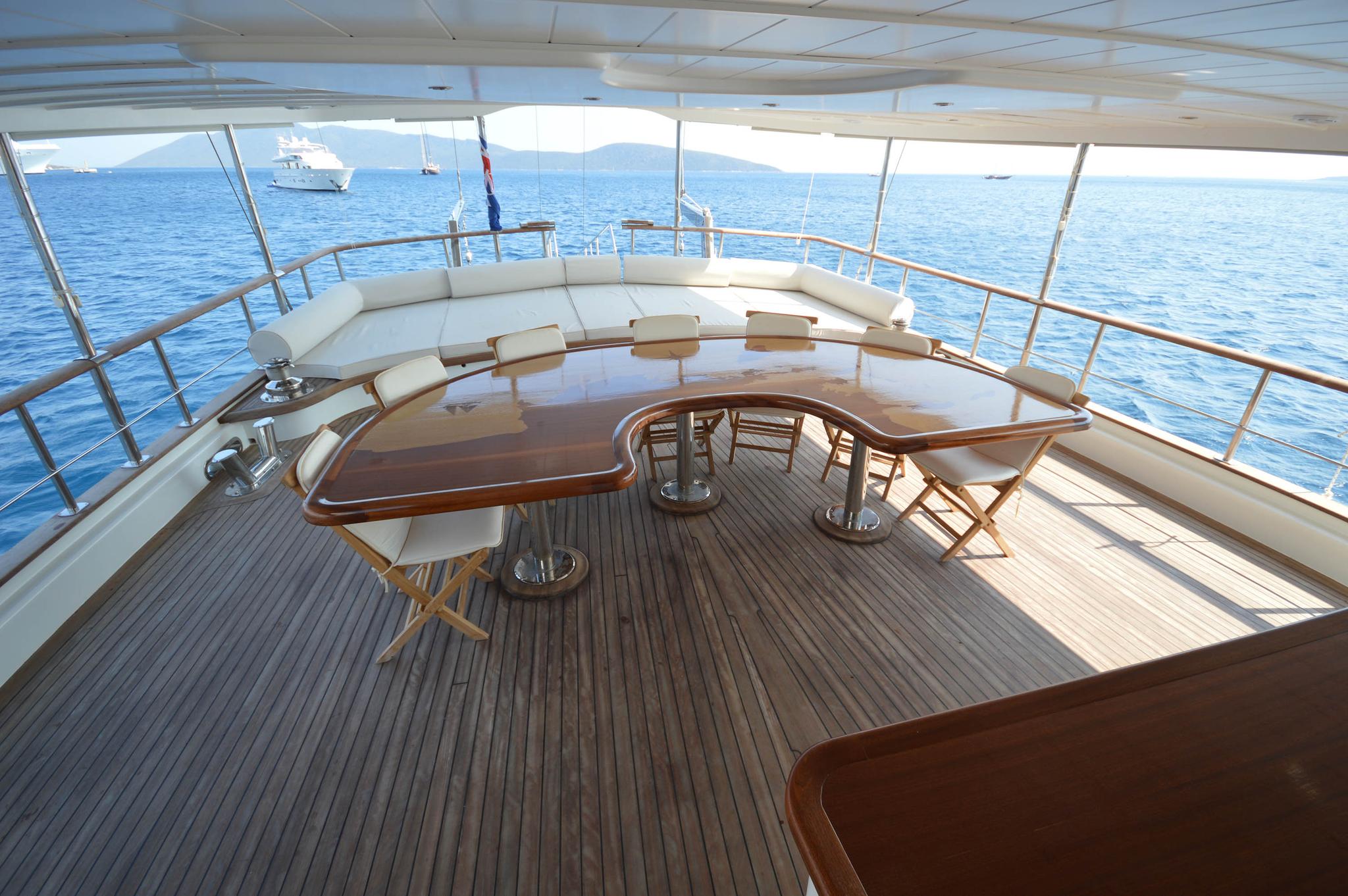 yacht upper deck with curved white banquette seating, wooden table and folding chairs