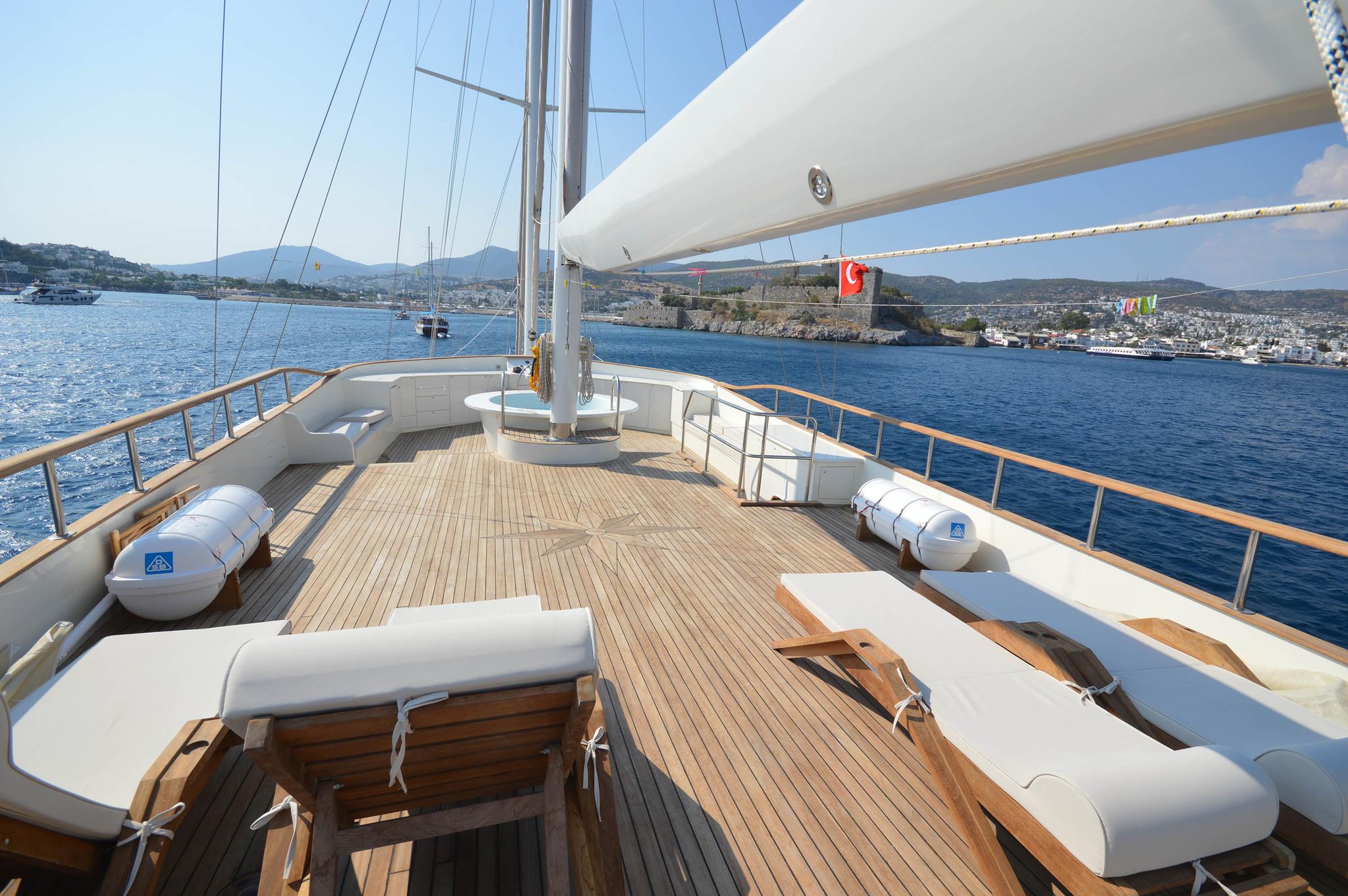 Gulet foredeck with curved white bench seating, teak decking, and stainless steel railings