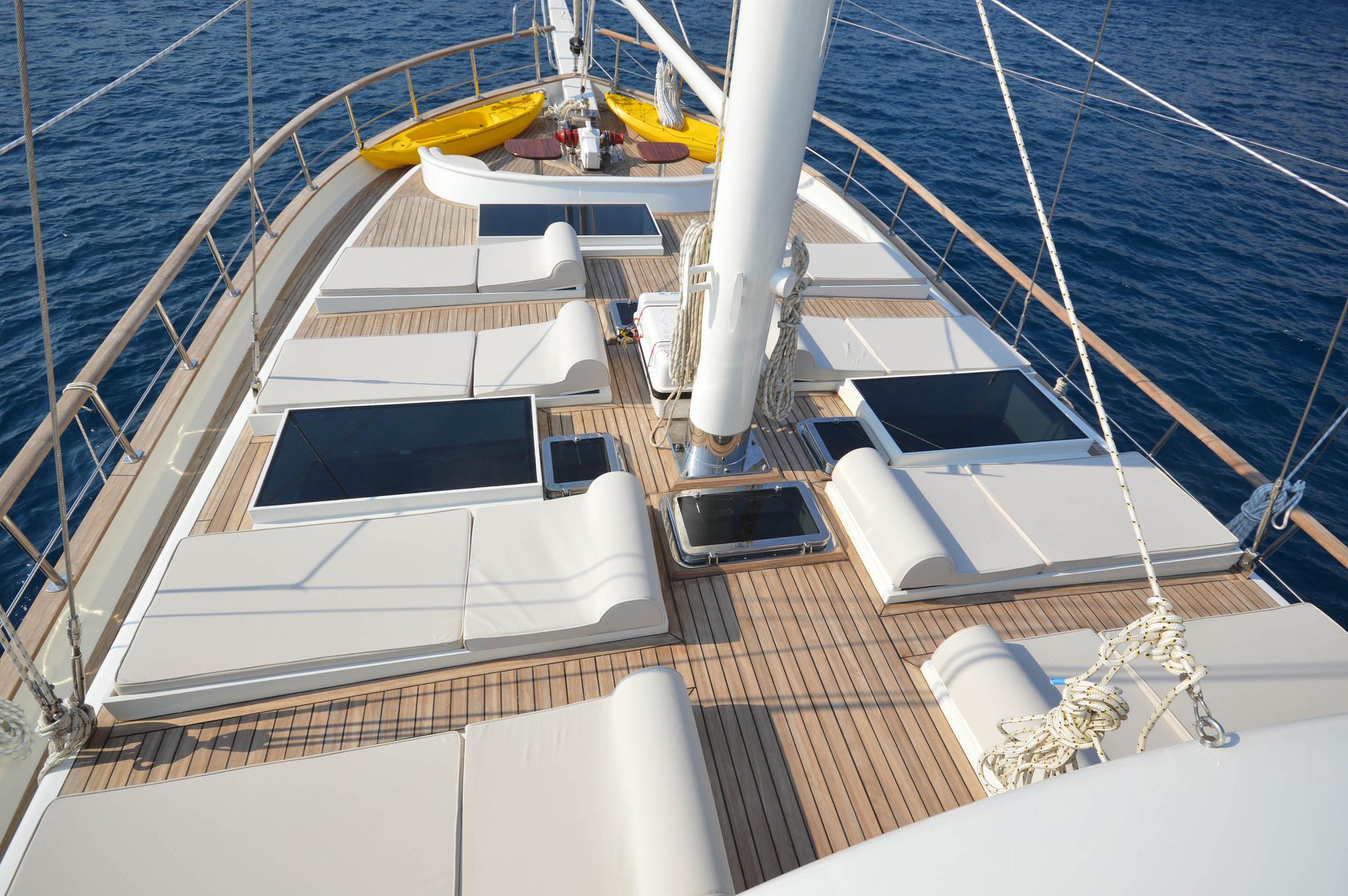 gulet forward deck with white sunpads, teak flooring, central mast and yellow kayaks