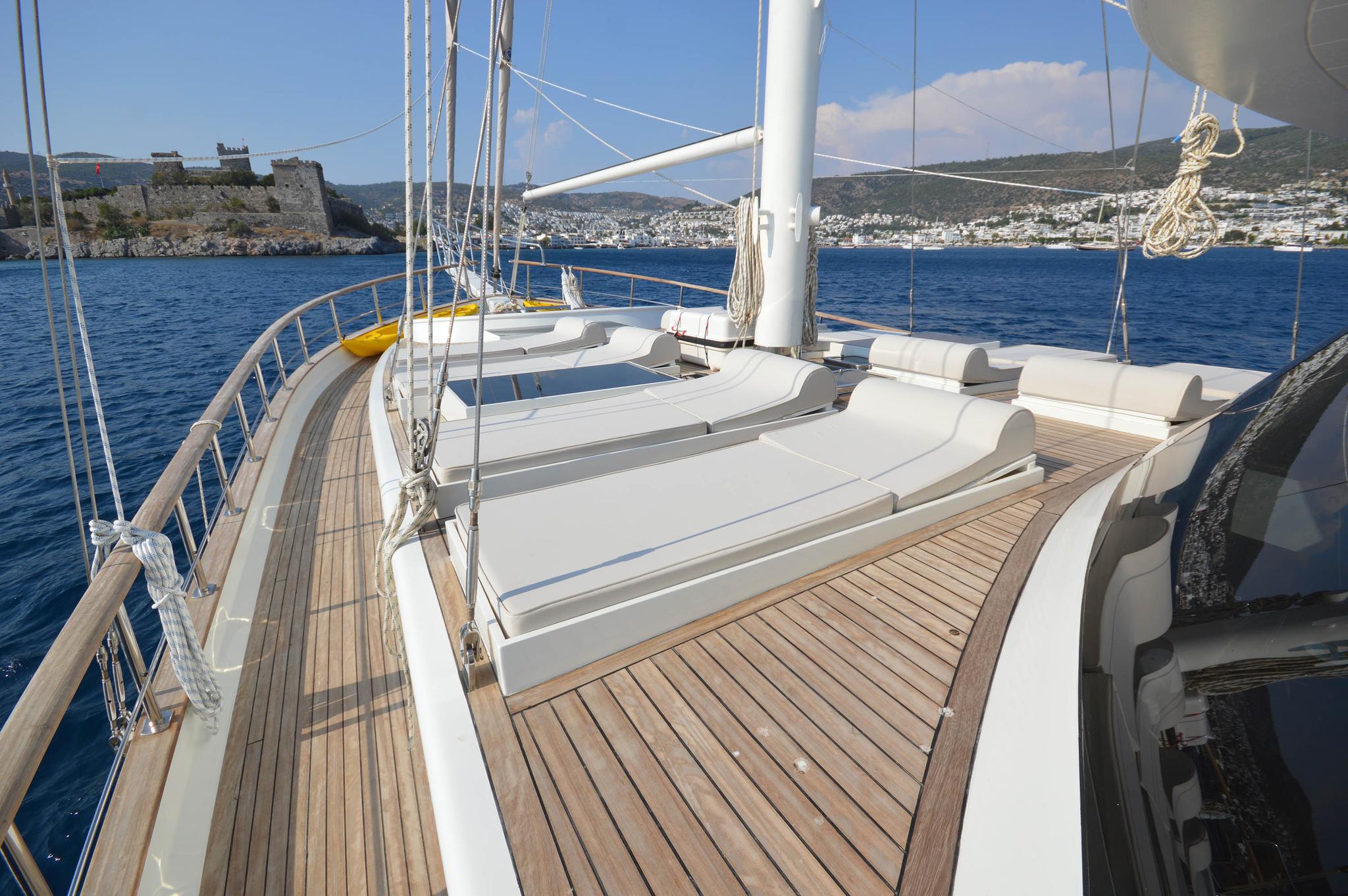 luxury yacht bow deck featuring white cushioned seating area and teak decking with coastal backdrop