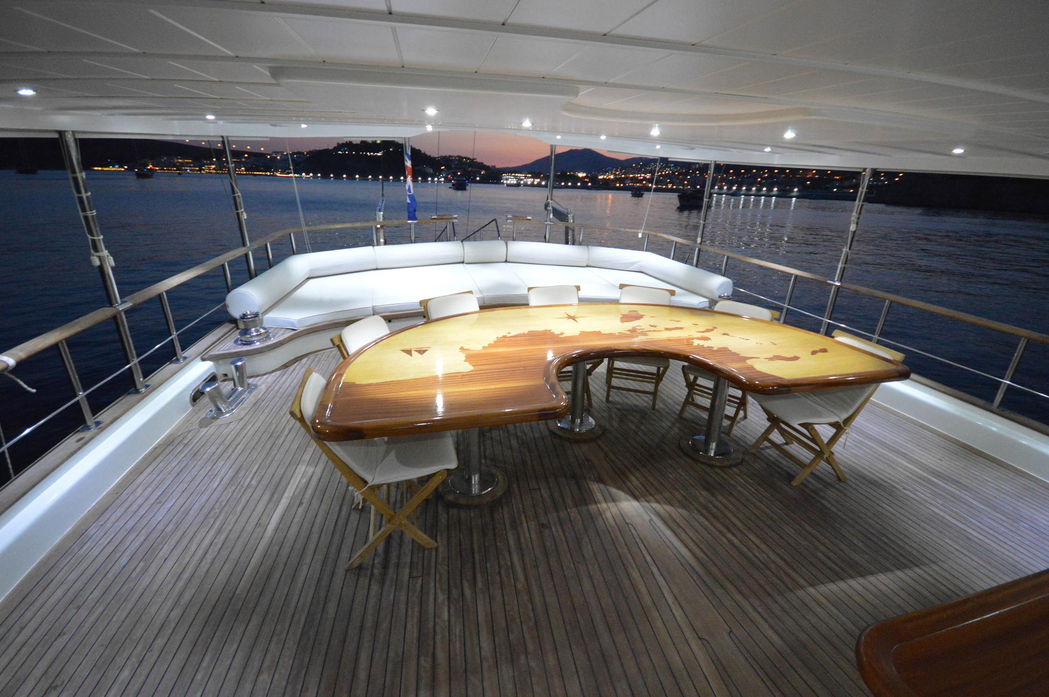 luxury yacht upper deck dining area with curved seating and wooden table at twilight